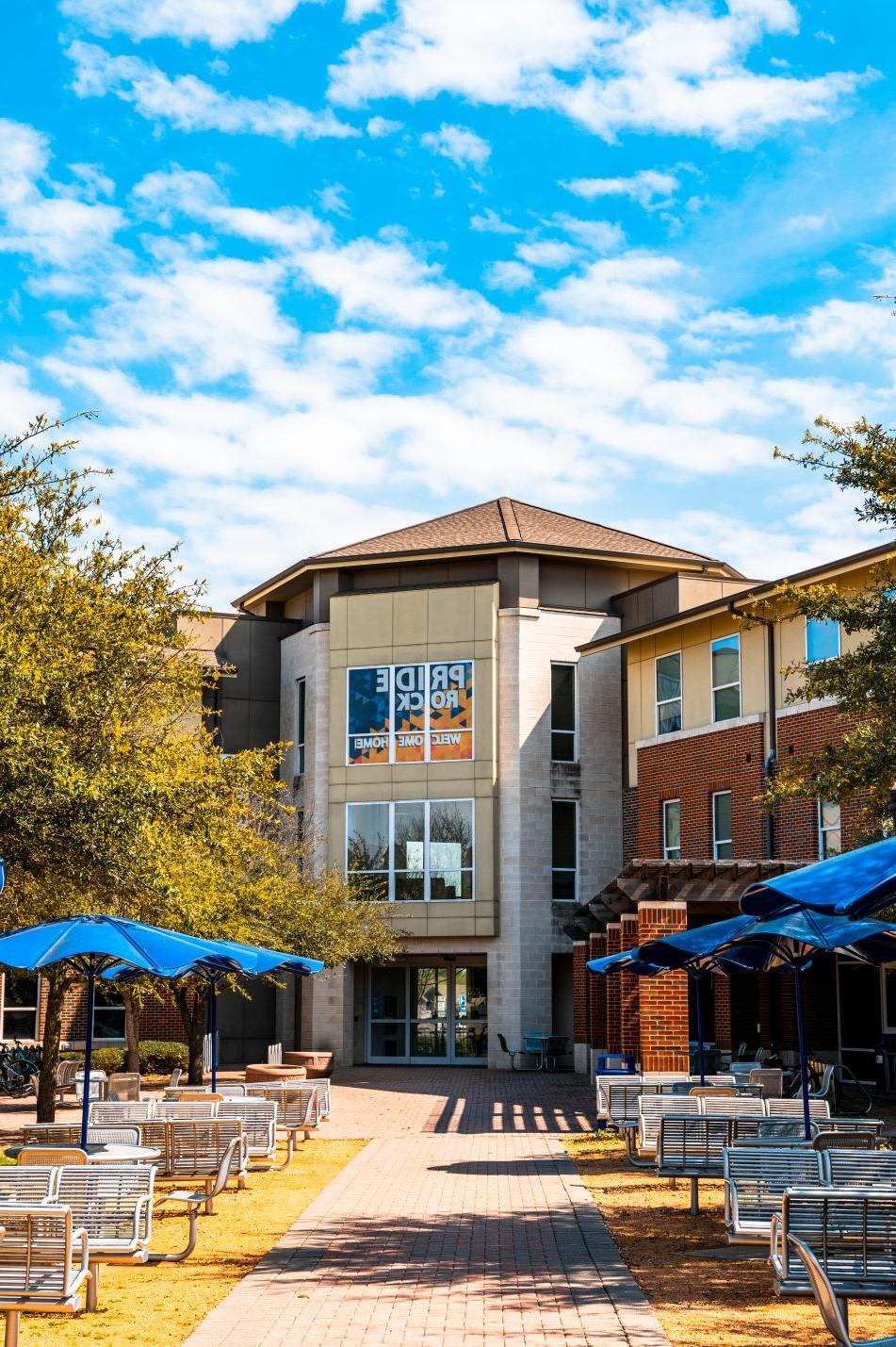 The Pride Rock residence hall at East Texas A&M University greets students with a welcoming sign, outdoor seating and shaded gathering spaces.